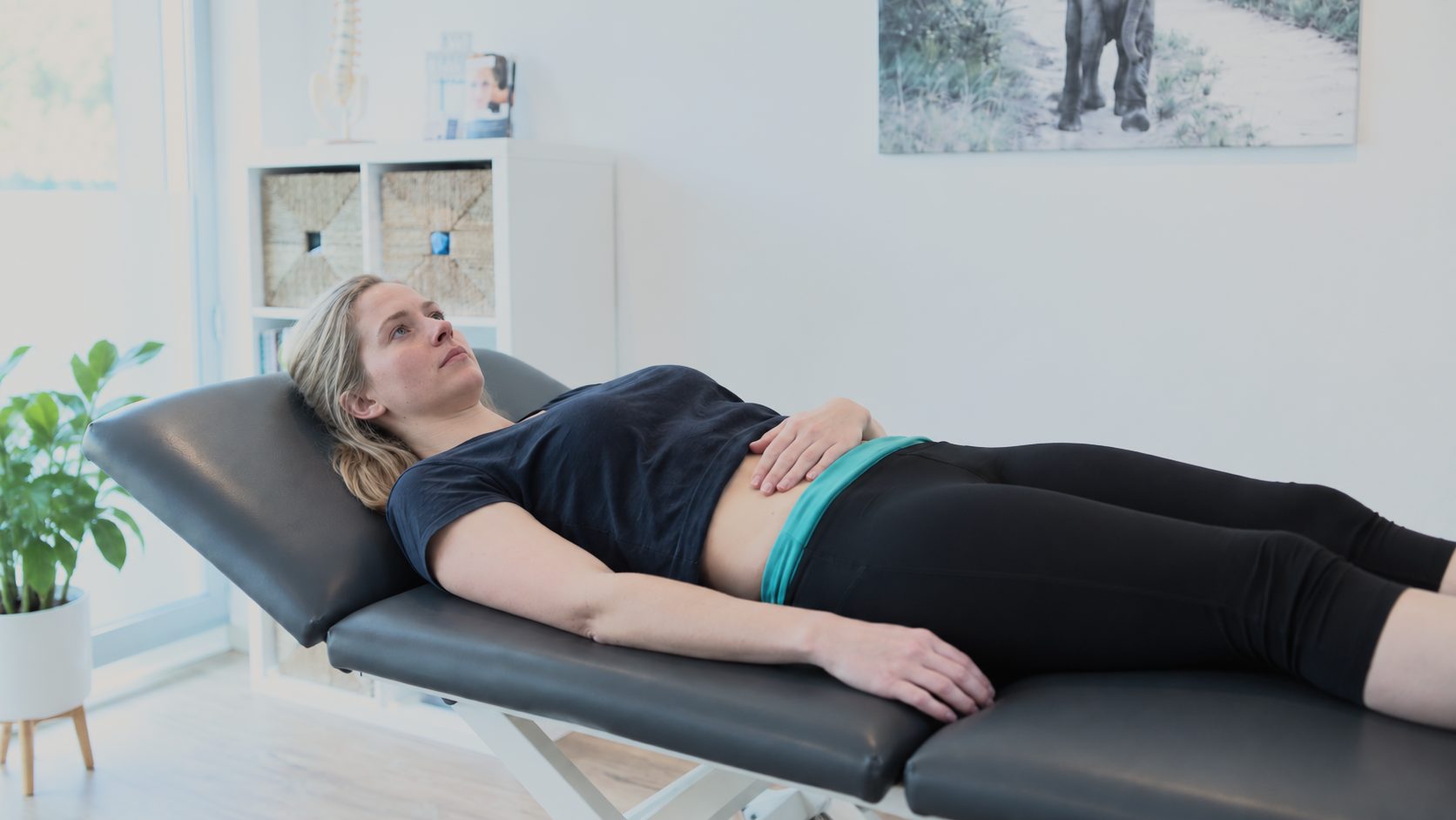 Patientin liegt ruhig auf der Behandlungsliege, eine Hand auf dem Unterbauch